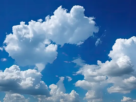 Ein strahlend blauer Himmel voller großer, flauschiger weißer Wolken unterschiedlicher Formen und Größen. Das Sonnenlicht beleuchtet die Wolken und erzeugt einen Kontrast zwischen dem strahlend weißen und dem tiefblauen Hintergrund.